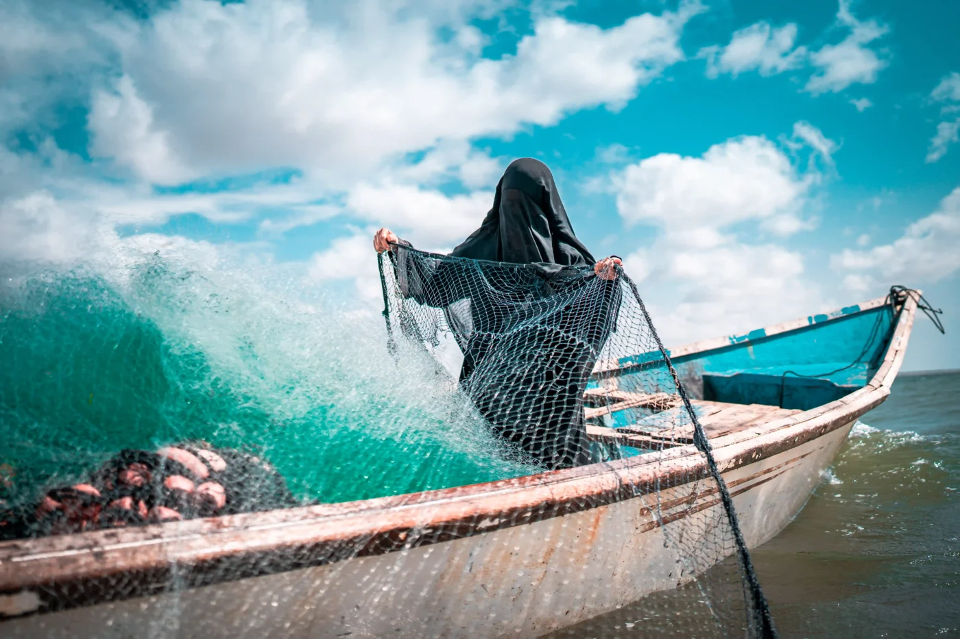 A woman in a fishing boat casting her net into the water